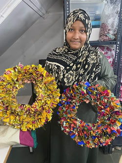 A Pri Pri worker holding two colourful upcycled sari wreaths